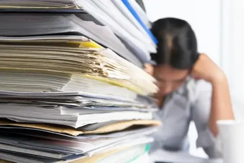 woman overwhelmed by pile of paperwork woman overwhelmed by pile of paperwork